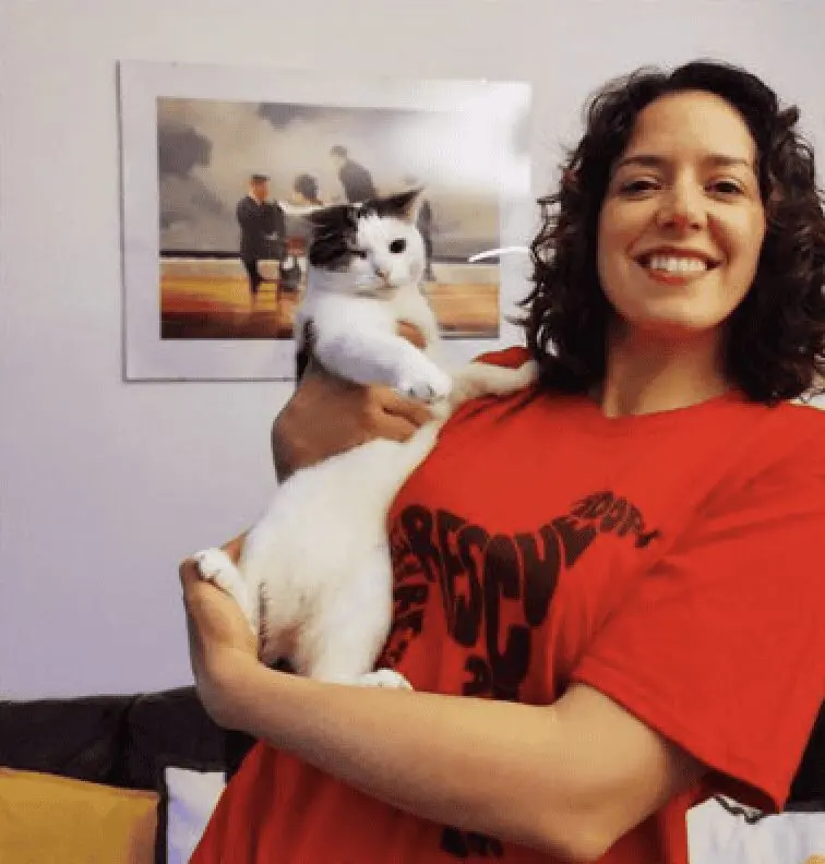 A photo of Paws2Rescue team member Anca wearing a red t-shirt and smiling while holding a black and white cat